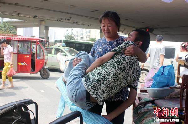 來(lái)到街頭“賣唱”點(diǎn)，呂愛(ài)梅熟練地把兒子把下三輪車，布置場(chǎng)地。 馬義恒 攝