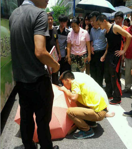 涉事公交車所屬公司相關負責人表示，事故原因警方正在調查中，該公司將會負責阿婆的醫藥費。圖為阿婆被抬出，有街坊給她撐起一把傘，等待救護車。目擊者供圖