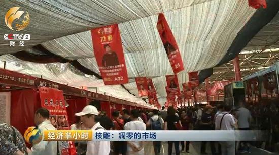 潘家園舊貨市場的這塊空地上，臨時支起了一些棚子和攤位，正在舉辦一個核雕展銷會。頂棚上方高高懸掛著前來參加展銷會的雕刻師的照片。