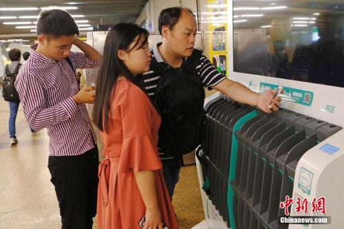 圖為沒帶雨傘的民眾在共享雨傘的貨架上掃碼借用。殷立勤 攝