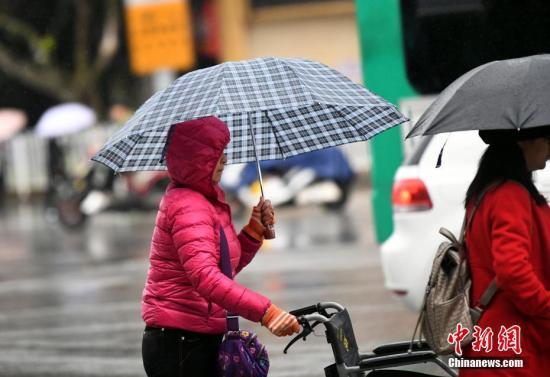 資料圖：昆明市區(qū)里身著羽絨服冒雨趕路的民眾。 中新社記者 李進紅 攝