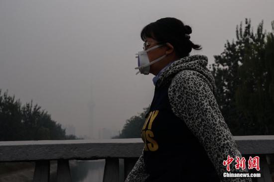 資料圖：北京一名市民戴防霾口罩在戶外行走，遠(yuǎn)處的中央電視塔亦被霧霾籠罩。<a target='_blank' href='http://www.chinanews.com/'>中新社</a>記者 崔楠 攝