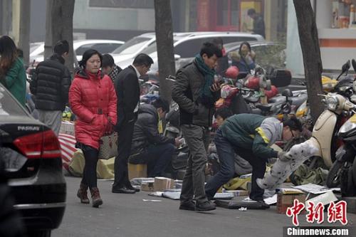 一家快遞公司的員工蹲在馬路邊分發(fā)郵件，身邊堆放著大量的包裹。 王中舉 攝 