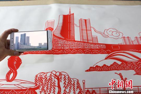 圖為丁健對比照片與剪紙作品。　夏瑩 攝