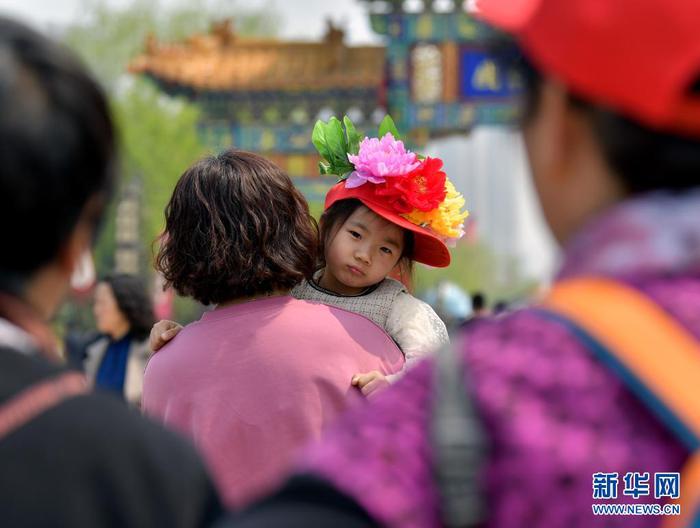 4月8日，一名頭戴“牡丹”花帽的小游客和家人一起游園。